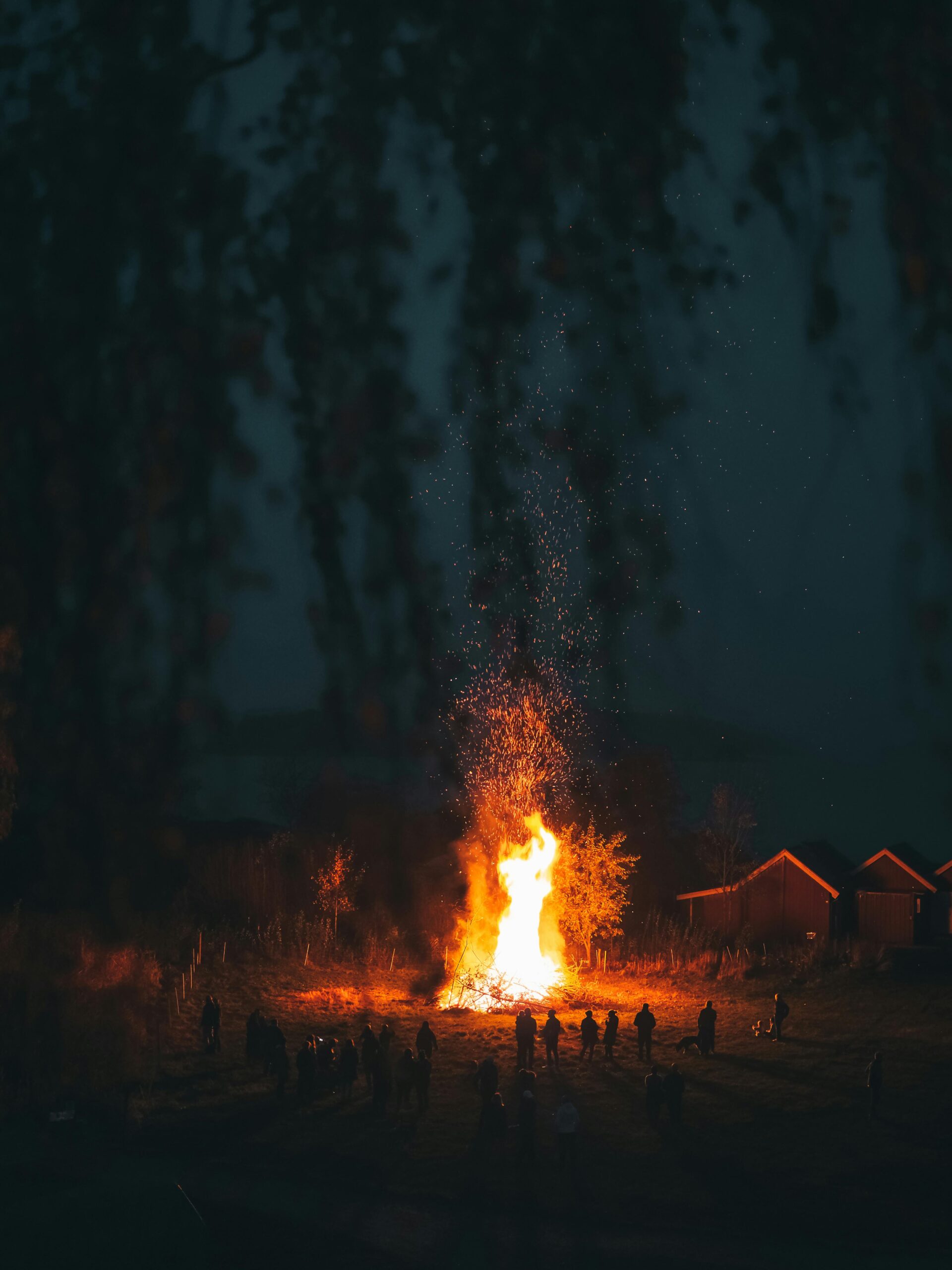 Large bonfire with people silhouetted against the night sky, creating a warm, communal atmosphere.